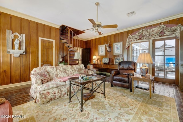 living room featuring ceiling fan, ornamental molding, and wood walls