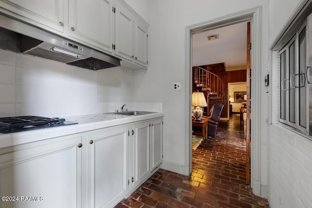 kitchen with stainless steel gas stovetop, white cabinetry, sink, and tile countertops