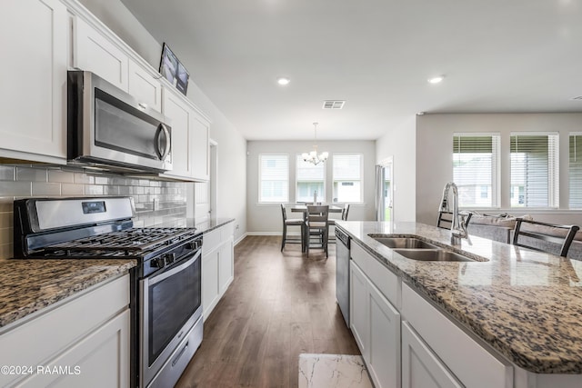 kitchen featuring a kitchen island with sink, stainless steel appliances, sink, white cabinets, and pendant lighting