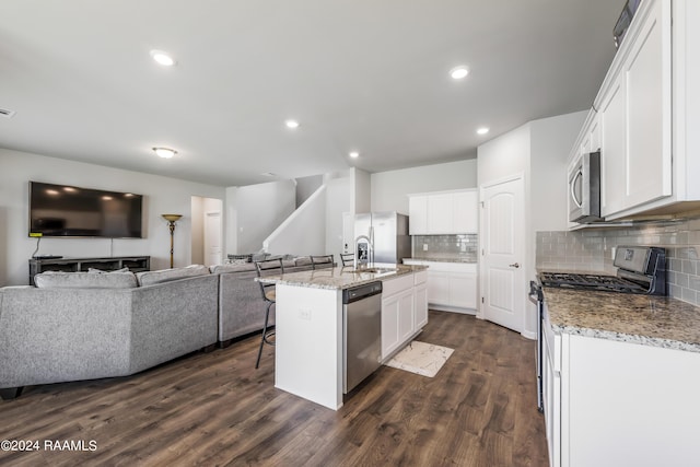 kitchen featuring dark wood-type flooring, stainless steel appliances, an island with sink, white cabinets, and a kitchen bar