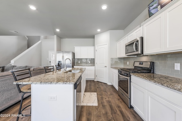 kitchen with a kitchen island with sink, sink, appliances with stainless steel finishes, white cabinets, and a kitchen bar