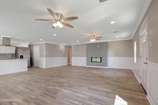 unfurnished living room with a large fireplace, a wainscoted wall, ceiling fan, and light wood-style flooring