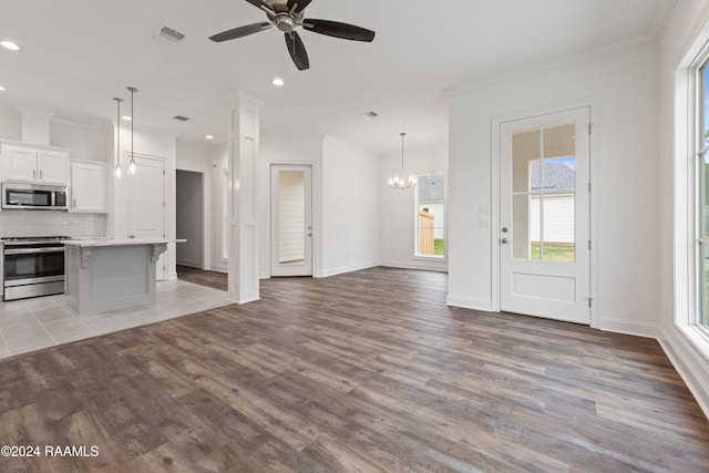 unfurnished living room featuring hardwood / wood-style flooring, ornamental molding, and ceiling fan with notable chandelier