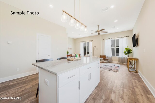 kitchen with wood-type flooring, ceiling fan, pendant lighting, white cabinets, and a center island