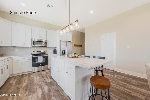 kitchen with appliances with stainless steel finishes, a center island, hardwood / wood-style flooring, and backsplash