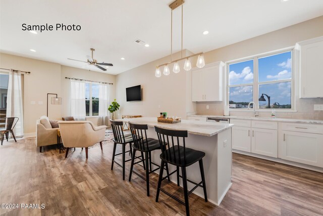 kitchen featuring decorative light fixtures, white cabinetry, wood-type flooring, a center island, and light stone counters