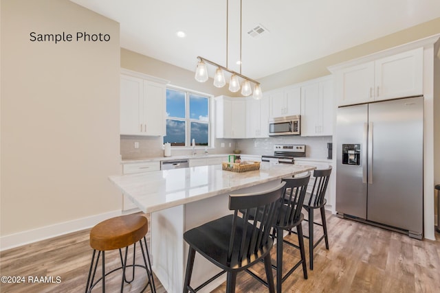 kitchen with white cabinetry, a center island, light hardwood / wood-style floors, appliances with stainless steel finishes, and decorative backsplash