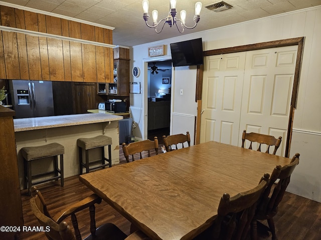 dining room featuring ceiling fan with notable chandelier, dark wood-type flooring, ornamental molding, and wood walls