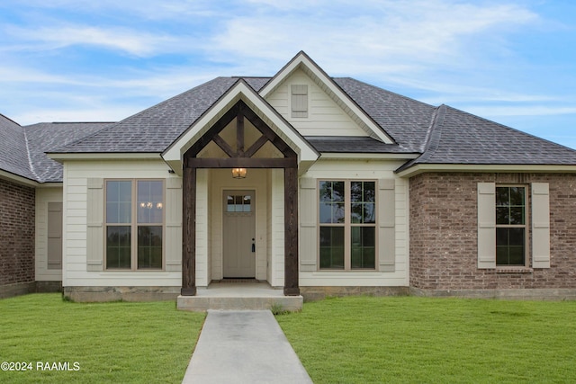 view of front of home featuring brick siding, a front lawn, and roof with shingles