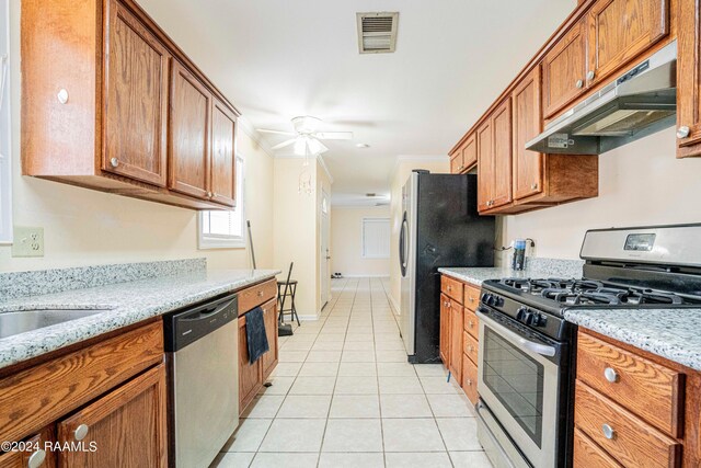 kitchen with light tile patterned flooring, stainless steel appliances, ceiling fan, and light stone countertops