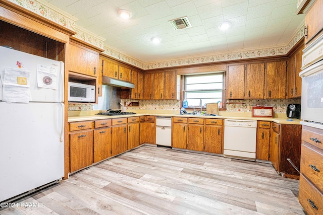 kitchen with sink, white appliances, decorative backsplash, and light wood-type flooring