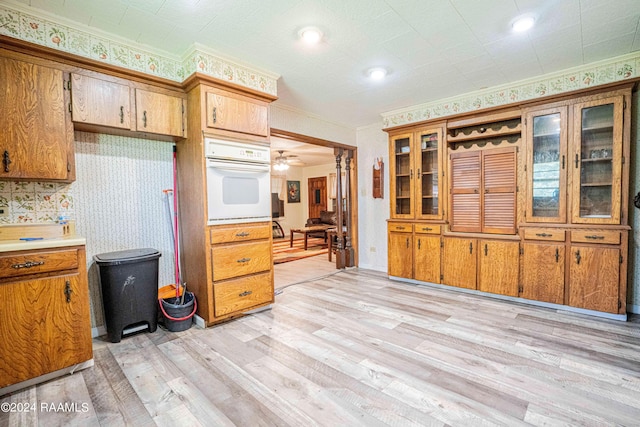 kitchen with ornamental molding, oven, and light wood-type flooring