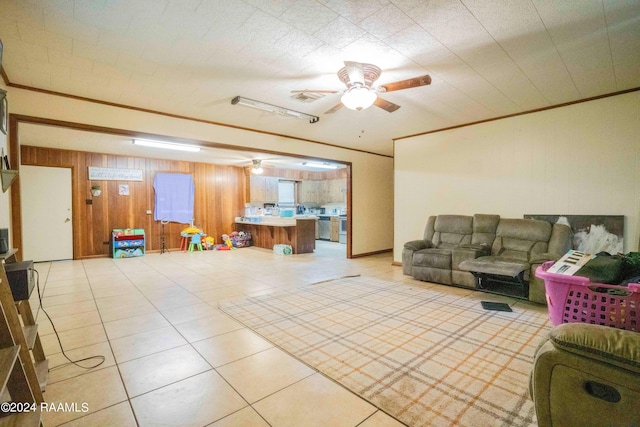 living room featuring light tile patterned flooring, ceiling fan, ornamental molding, and wooden walls