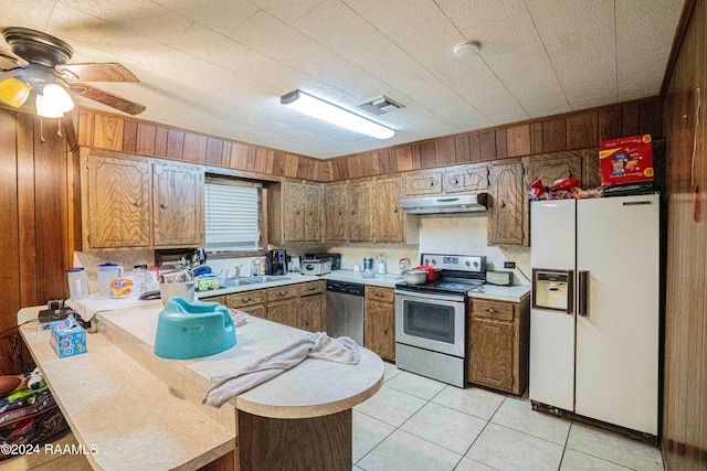 kitchen featuring light tile patterned flooring, sink, wooden walls, kitchen peninsula, and stainless steel appliances