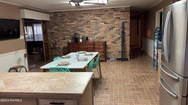 kitchen featuring a center island, a wainscoted wall, crown molding, brick patterned floor, and freestanding refrigerator