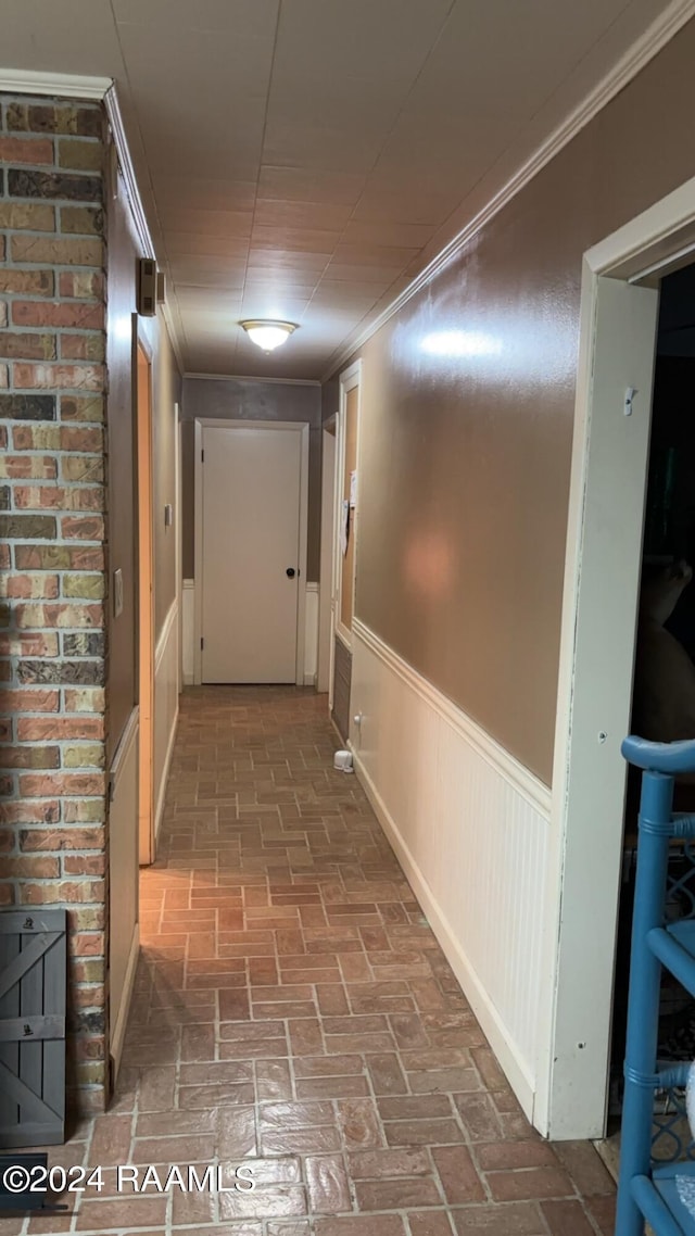 corridor with brick floor, ornamental molding, and wainscoting