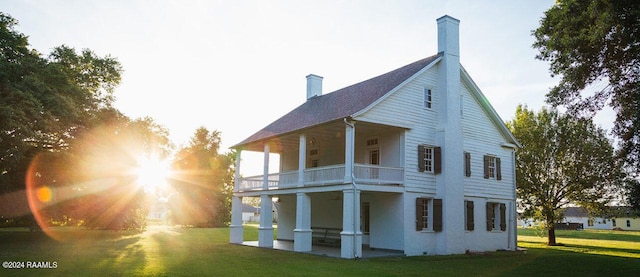 rear view of house featuring a balcony, a chimney, a patio, and a yard