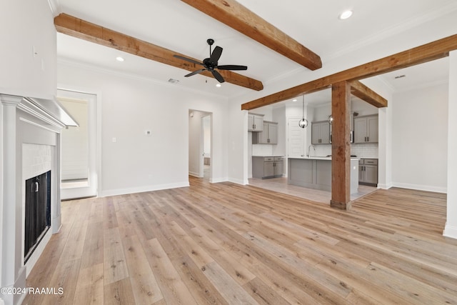 unfurnished living room featuring a fireplace, baseboards, ornamental molding, beam ceiling, and light wood finished floors