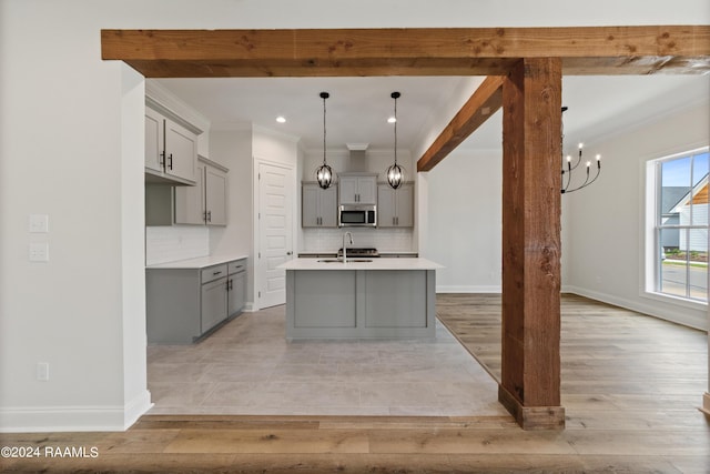 kitchen with gray cabinets, stainless steel microwave, ornamental molding, a sink, and an island with sink