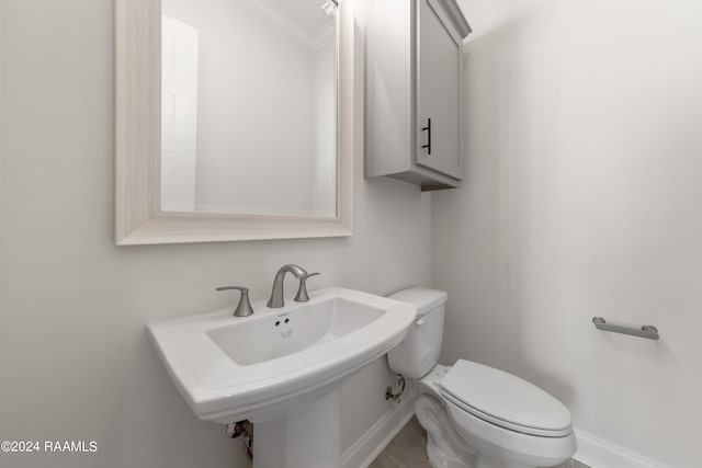 half bathroom with toilet, crown molding, baseboards, and a sink