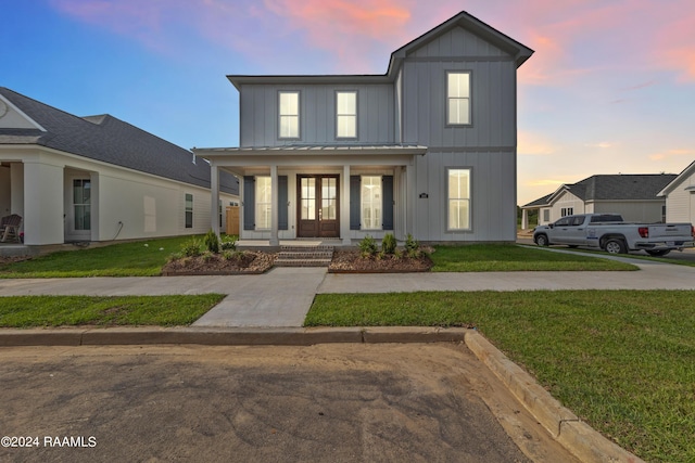 view of front of house with french doors, a porch, board and batten siding, a front yard, and a standing seam roof