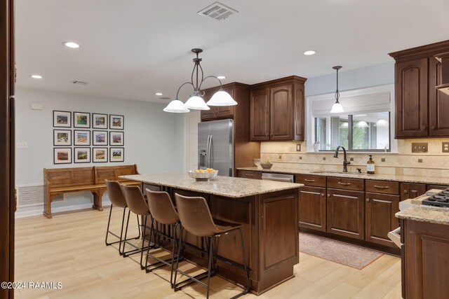 kitchen with pendant lighting, a center island, stainless steel appliances, sink, and light wood-type flooring