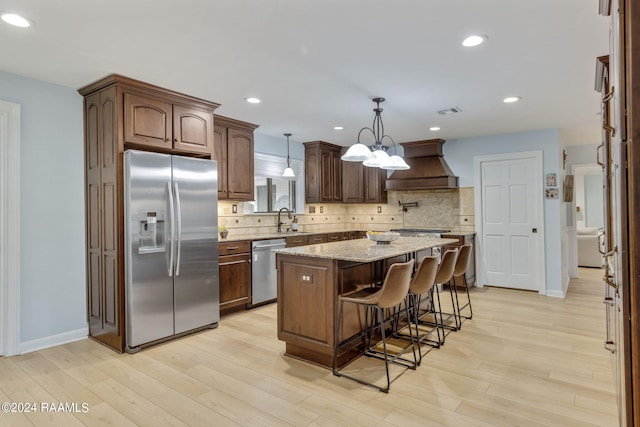 kitchen with a center island, custom range hood, light hardwood / wood-style flooring, decorative light fixtures, and stainless steel appliances