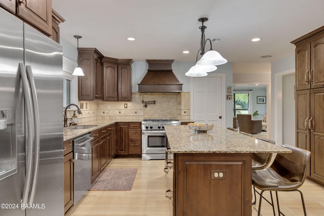 kitchen featuring light wood-type flooring, stainless steel appliances, a center island, premium range hood, and sink