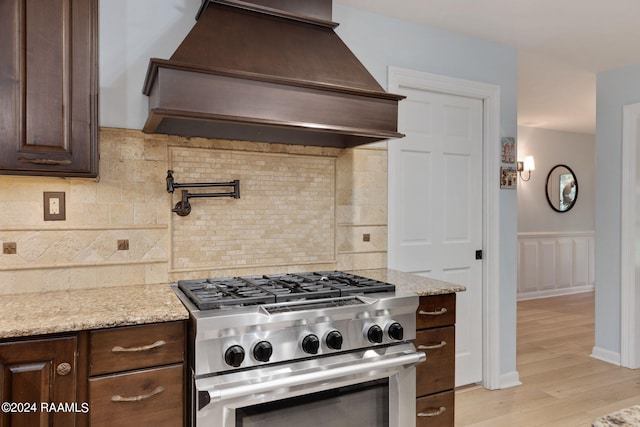 kitchen with high end stainless steel range oven, dark brown cabinetry, backsplash, and custom range hood