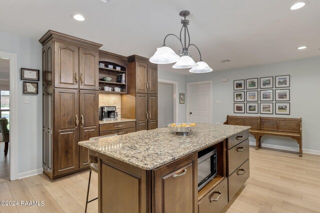 kitchen featuring pendant lighting, light hardwood / wood-style flooring, a center island, light stone counters, and stainless steel microwave