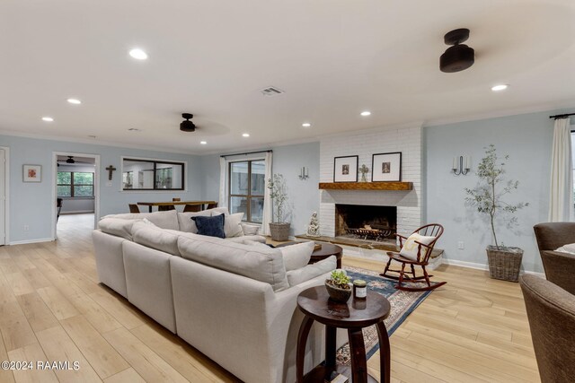 living room featuring ceiling fan, a fireplace, light hardwood / wood-style floors, and crown molding