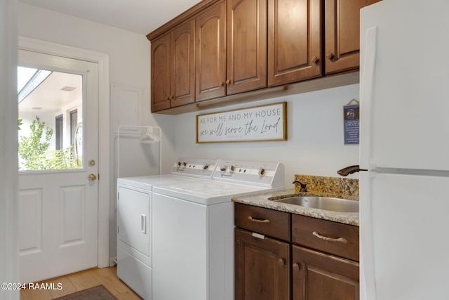 clothes washing area with cabinets, light hardwood / wood-style floors, washer and clothes dryer, and sink