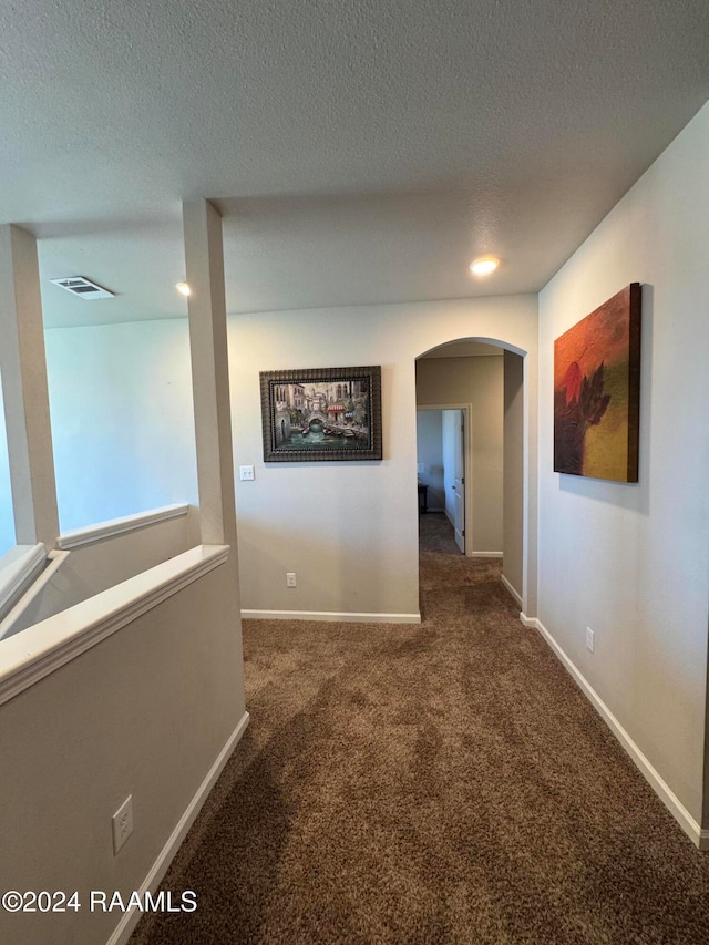 corridor featuring dark carpet and a textured ceiling