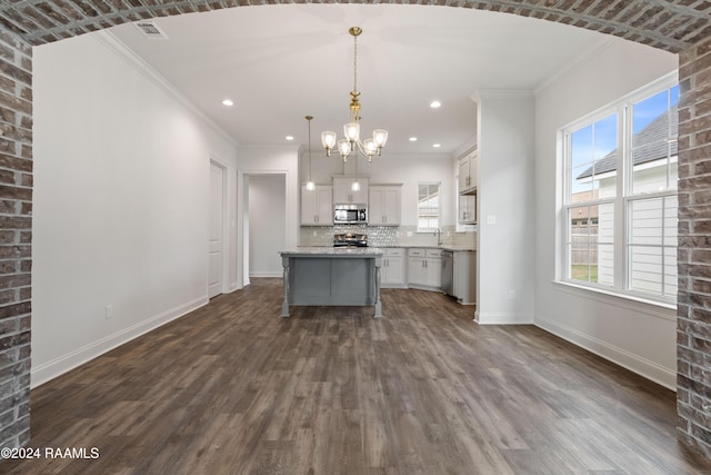 kitchen featuring appliances with stainless steel finishes, tasteful backsplash, decorative light fixtures, a center island, and dark wood-type flooring