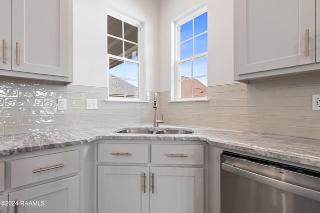 kitchen featuring white cabinetry, sink, light stone countertops, backsplash, and stainless steel dishwasher