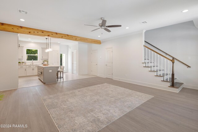 unfurnished living room featuring beam ceiling, ceiling fan, sink, and light hardwood / wood-style floors