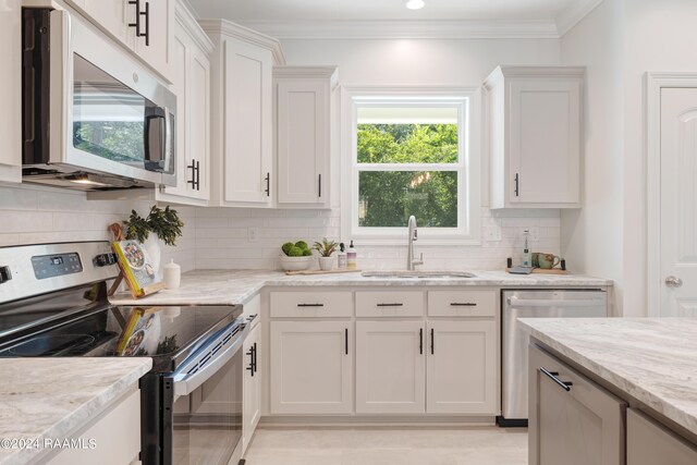 kitchen with appliances with stainless steel finishes, white cabinetry, light stone counters, sink, and decorative backsplash