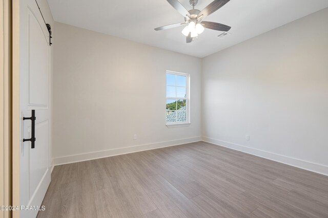 unfurnished room featuring ceiling fan, a barn door, and light hardwood / wood-style floors