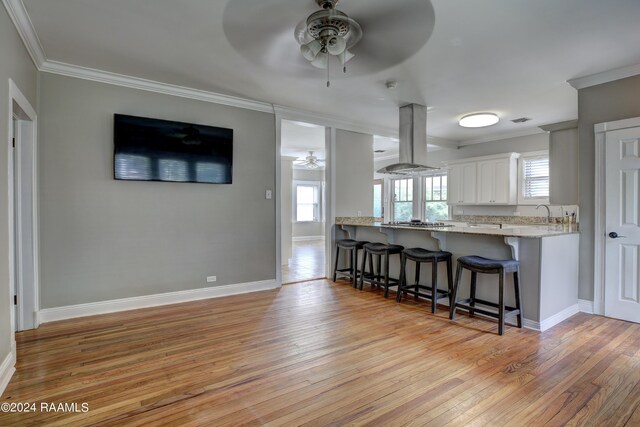 kitchen featuring a breakfast bar, white cabinetry, ornamental molding, kitchen peninsula, and island exhaust hood