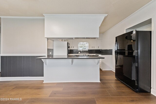 kitchen with crown molding, a breakfast bar area, black refrigerator, white cabinets, and dark hardwood / wood-style flooring