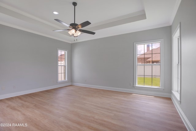 empty room with ornamental molding, ceiling fan, light wood-type flooring, and a tray ceiling