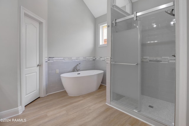 bathroom with separate shower and tub, hardwood / wood-style flooring, vaulted ceiling, and tile walls