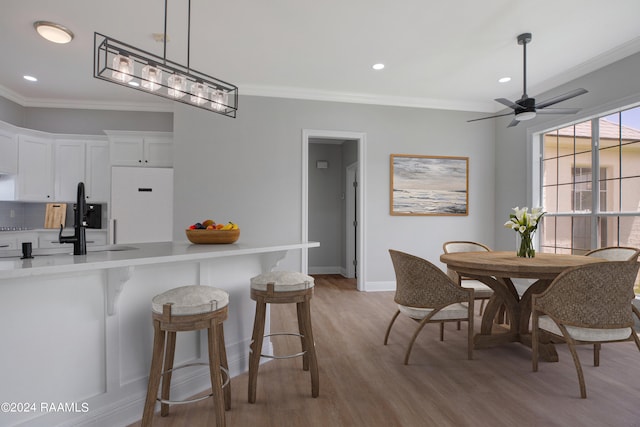 dining space featuring sink, ornamental molding, ceiling fan, and light hardwood / wood-style floors