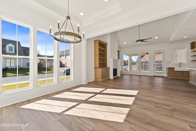 unfurnished living room featuring hardwood / wood-style flooring, a tray ceiling, ceiling fan with notable chandelier, and crown molding