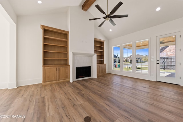 unfurnished living room featuring a healthy amount of sunlight, beam ceiling, a tiled fireplace, and light hardwood / wood-style flooring