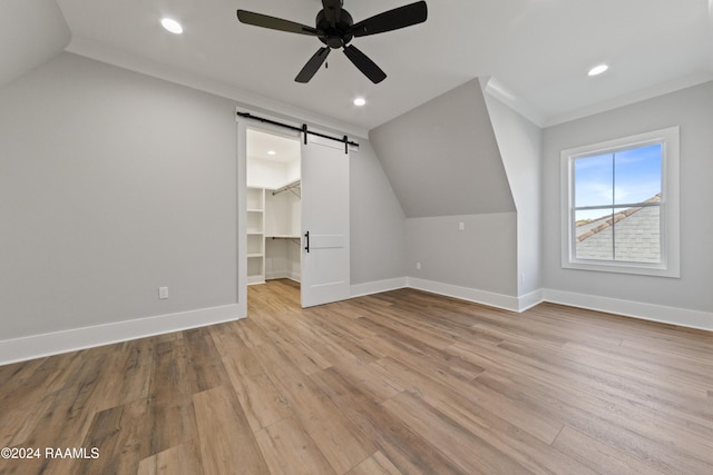 additional living space featuring lofted ceiling, a barn door, ceiling fan, and light wood-type flooring