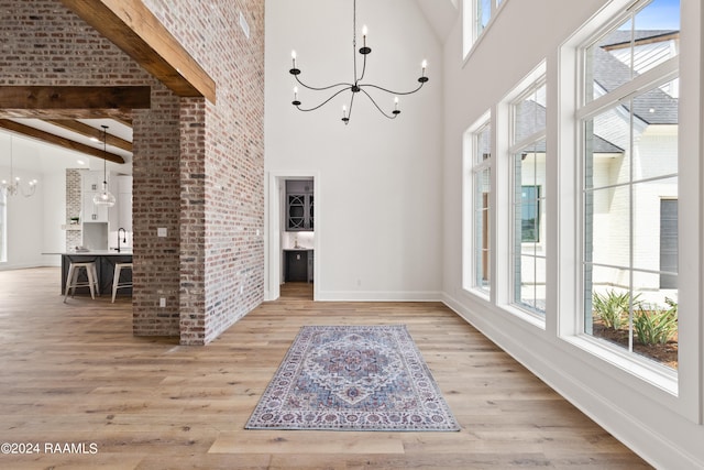 foyer entrance featuring light wood-type flooring, an inviting chandelier, beamed ceiling, sink, and a high ceiling