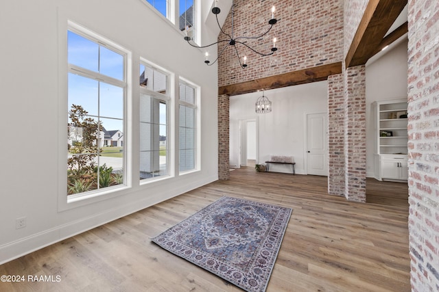 interior space featuring a towering ceiling, light wood-type flooring, beam ceiling, and an inviting chandelier