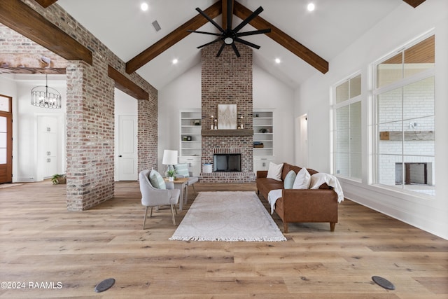 unfurnished living room with built in shelves, ceiling fan with notable chandelier, a brick fireplace, high vaulted ceiling, and beamed ceiling