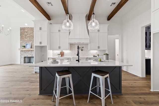 kitchen featuring custom exhaust hood, white cabinetry, a brick fireplace, light hardwood / wood-style floors, and beamed ceiling